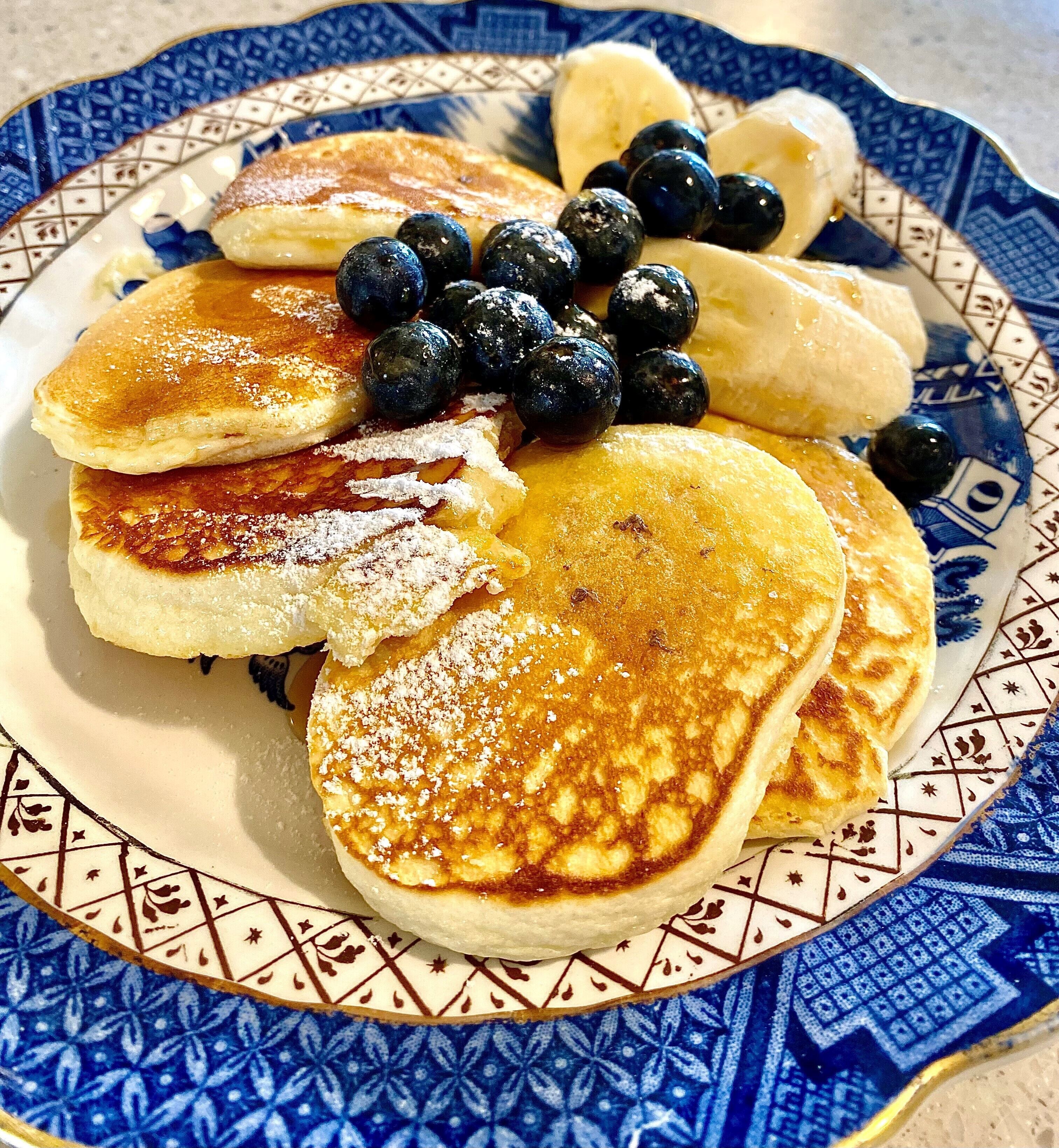 Un plato de tortitas con arándanos y plátanos, servido en un plato decorativo.