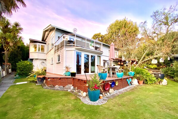Ein zweigeschossiges Haus mit Balkon, umgeben von einem gepflegten Garten mit verschiedenen Blumentöpfen.