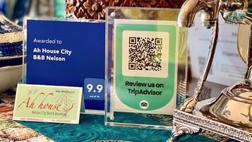 Una mesa con un plato decorativo, un letrero de Ah House City B&B, un código QR de TripAdvisor y una lámpara de latón.