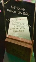 Una placa de reconocimiento enmarcada para AH House Nelson City B&B, que destaca su distinción como el Mejor Establecimiento de Alojamiento en los Premios Nelson a la Hospitalidad.