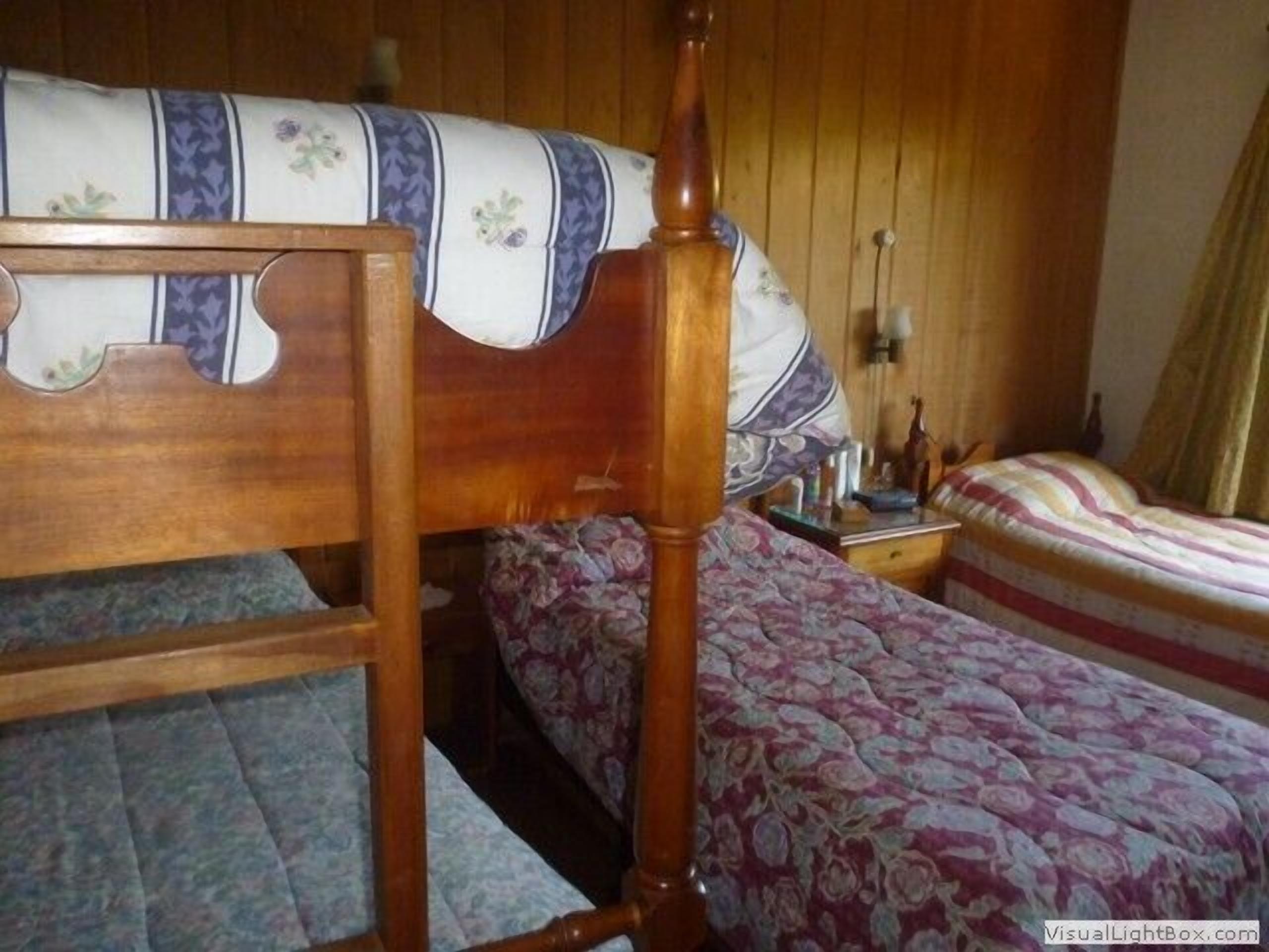 Una cama de madera con cabecera, una mesita de noche con lámpara, y una colcha con estampado floral.