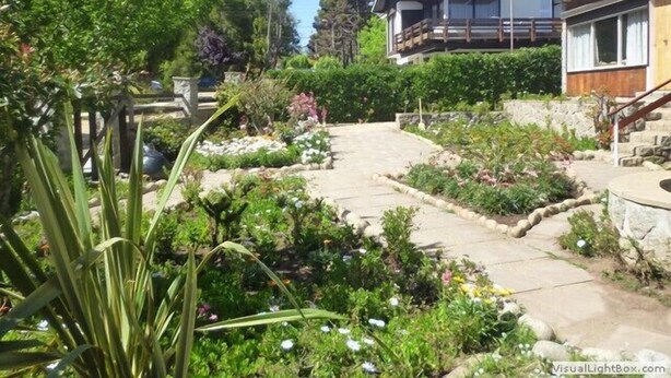 Un quartier résidentiel avec un sentier de pierre menant à une maison dotée d’une terrasse en bois et d’un mur en pierre.
