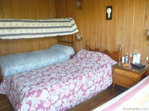 A room with two beds, wooden walls, a nightstand with toiletries, and a wall-mounted light fixture. - Casa Pescadores Poniente Algarrobo 1030 (Algarrobo)