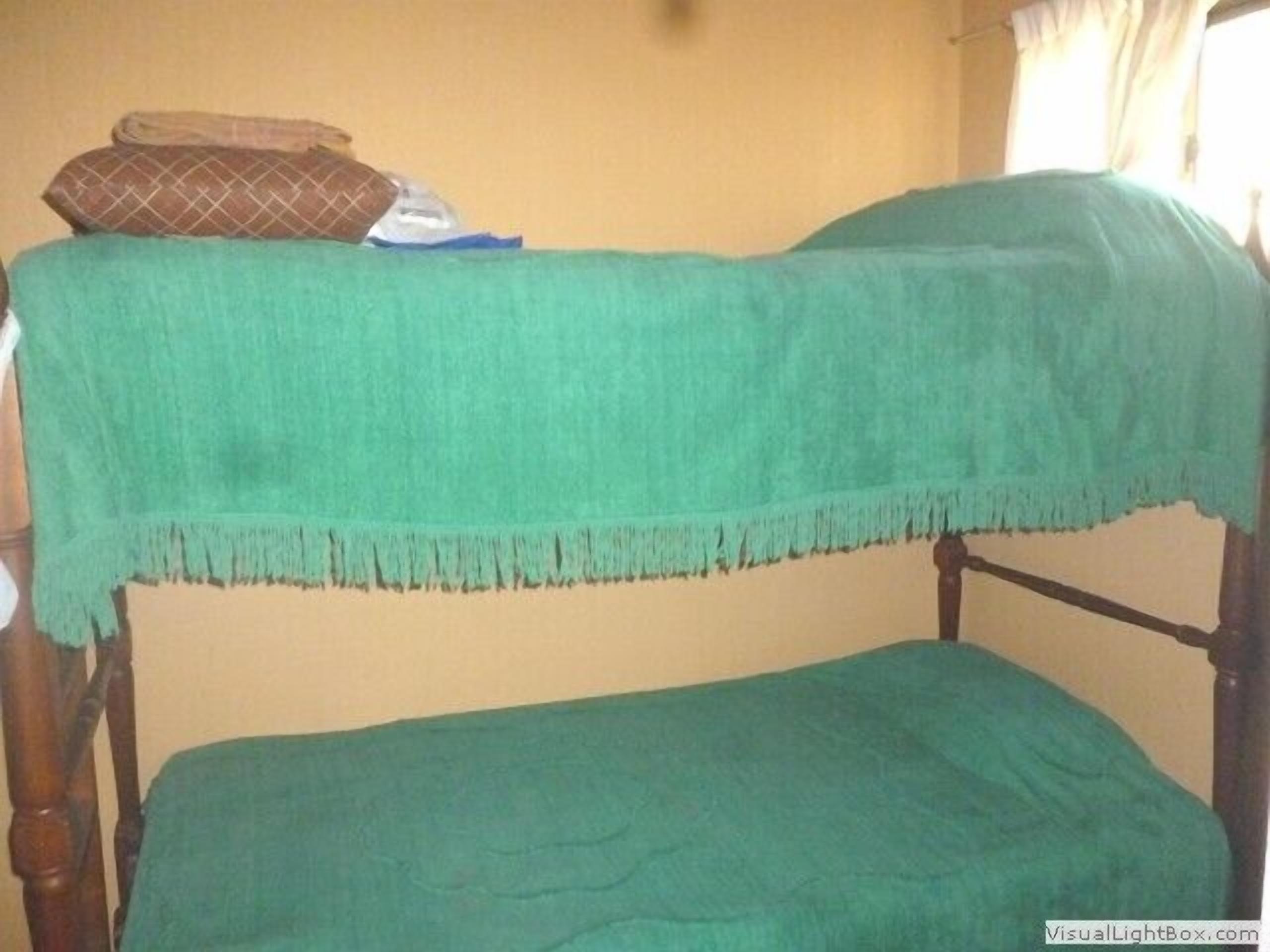 Una cama litera con una manta verde y un cojín marrón encima.