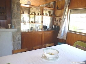 Uma área de refeições com uma mesa posta para dois, armários de madeira e uma parede de pedra.