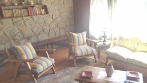 Un salon chaleureux avec un mur en pierre, deux fauteuils à rayures, un banc et une table basse agrémentée d’un vase et d’un livre.