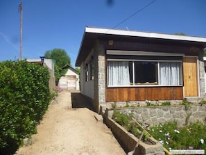 Uma casa térrea com fachada de pedra, varanda da frente de madeira e porta de garagem visível.