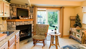Una sala de estar acogedora con chimenea, pared de piedra, muebles de madera y vistas al exterior.