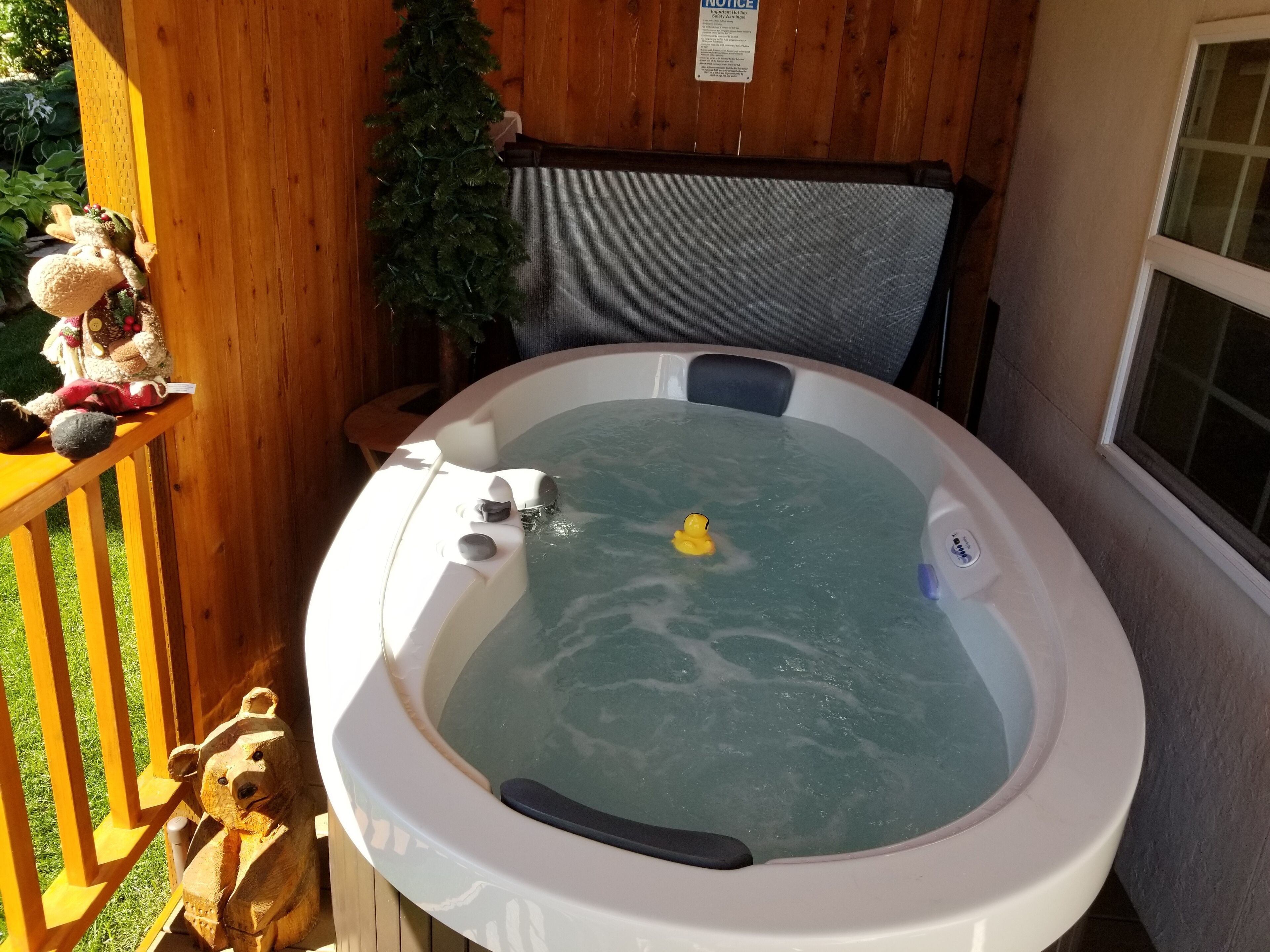 Un bain à remous avec une terrasse en bois, un ours en peluche en guise de décoration et un canard en caoutchouc jaune.