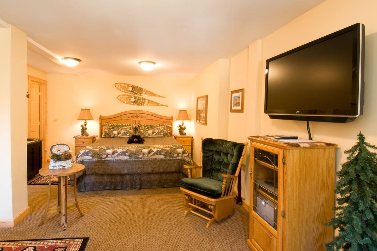 A bedroom with a bed, a chair, a TV, a cabinet, and a small Christmas tree.