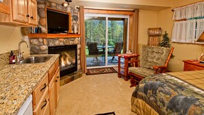 Una habitación acogedora con chimenea de piedra, televisor, comedor con sillas y cama con edredón estampado de flores.