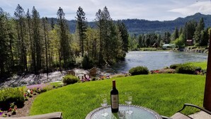 Un patio con una mesa y sillas de vidrio que da a un río y montañas boscosas.