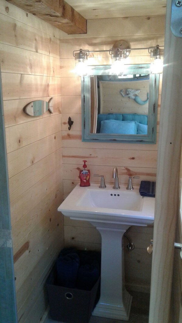 Un baño pequeño con paredes de madera, un lavamanos blanco, un espejo y un perchero para toallas.