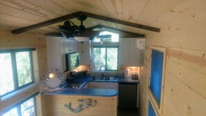 Eine kleine Küche mit Herd, Mikrowelle und Spüle, Holzwänden und einem Fenster, das für natürliches Licht sorgt.