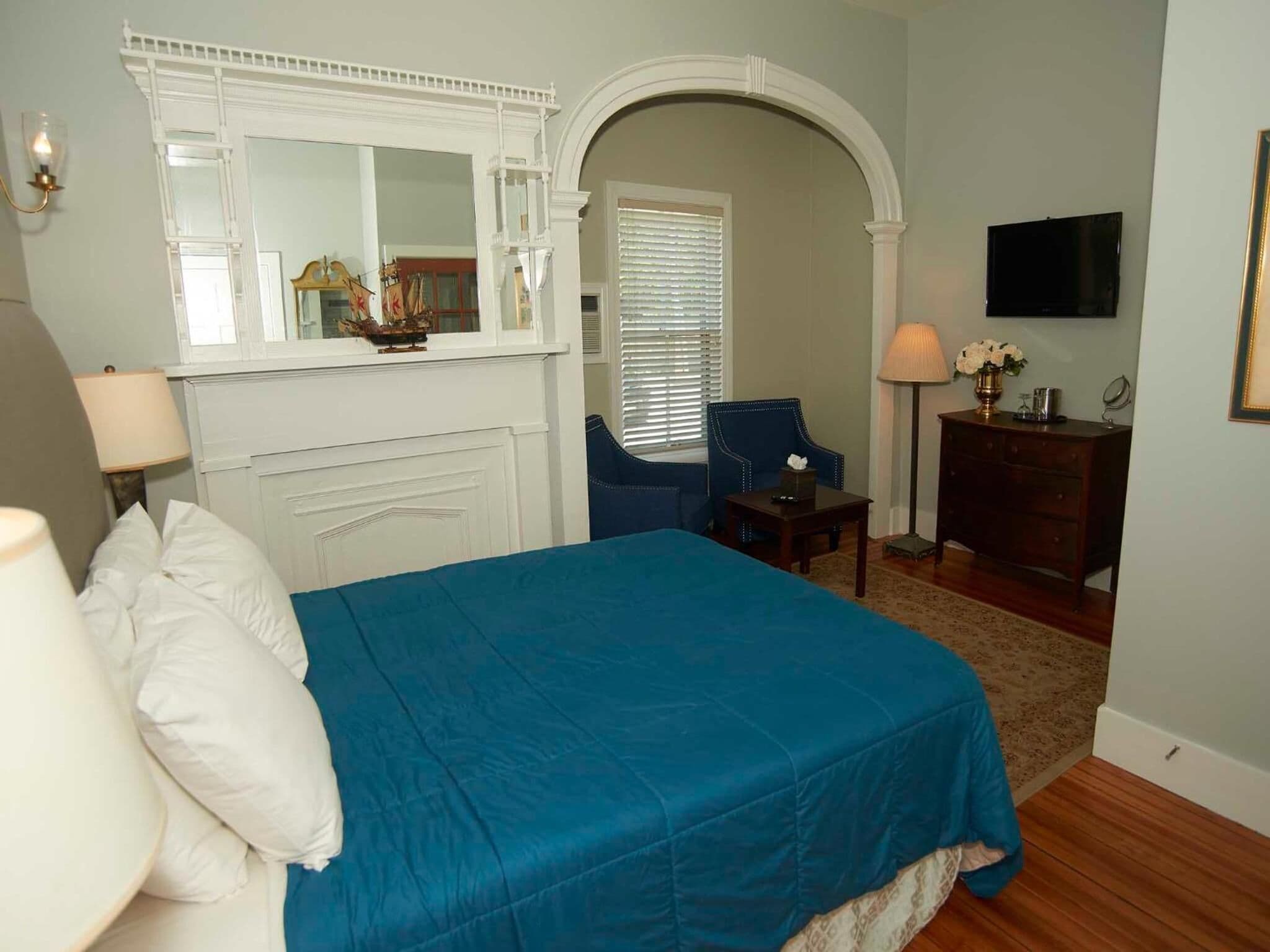 A bedroom with a bed, a chair, a dresser, a TV, and a mirror.