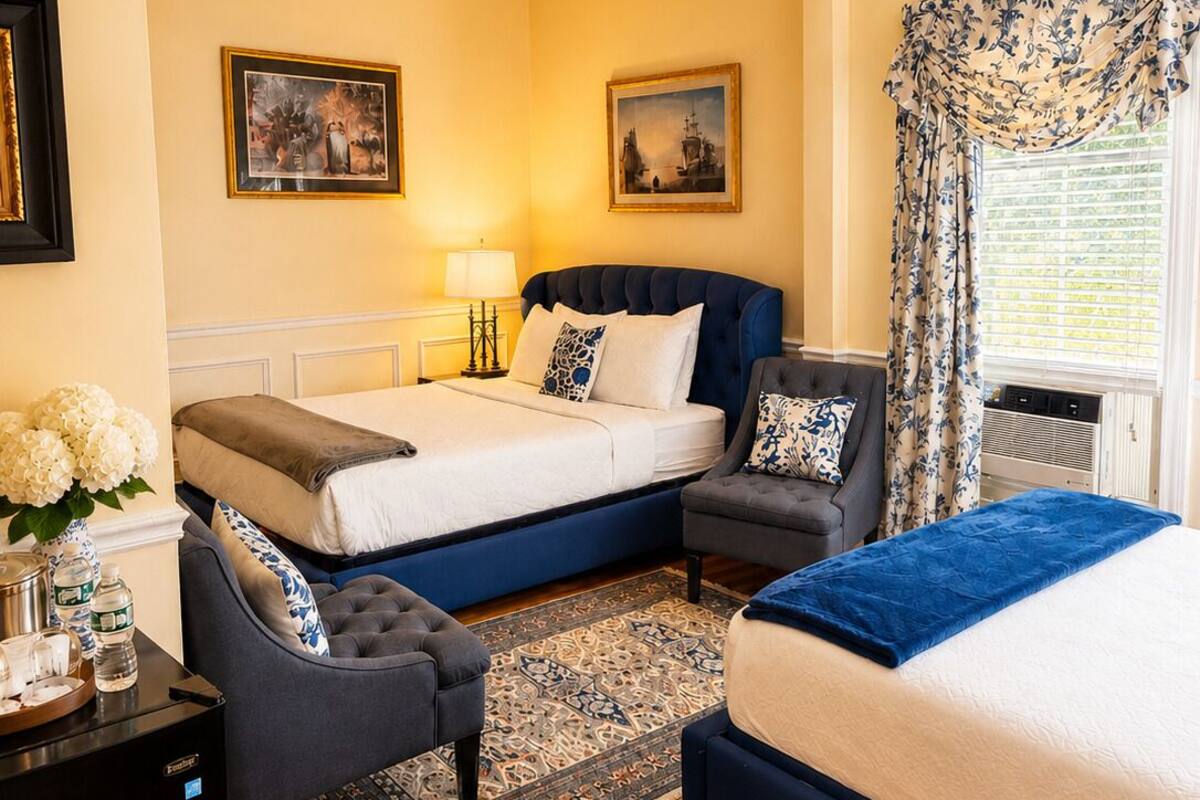 A bedroom with a double bed, a sofa, a small table with a vase and bottles, and two framed pictures on the wall.