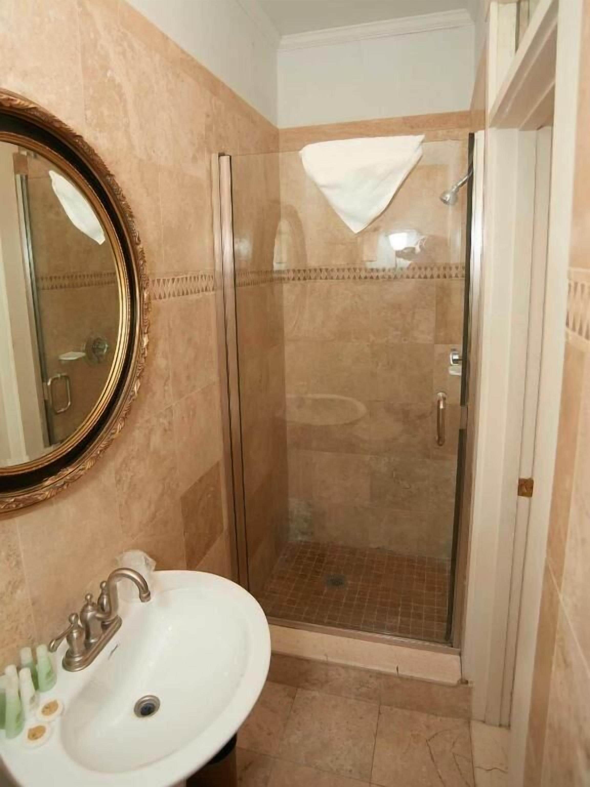 Un baño con ducha de vidrio, lavamanos con artículos de aseo y espejo con un marco decorativo.