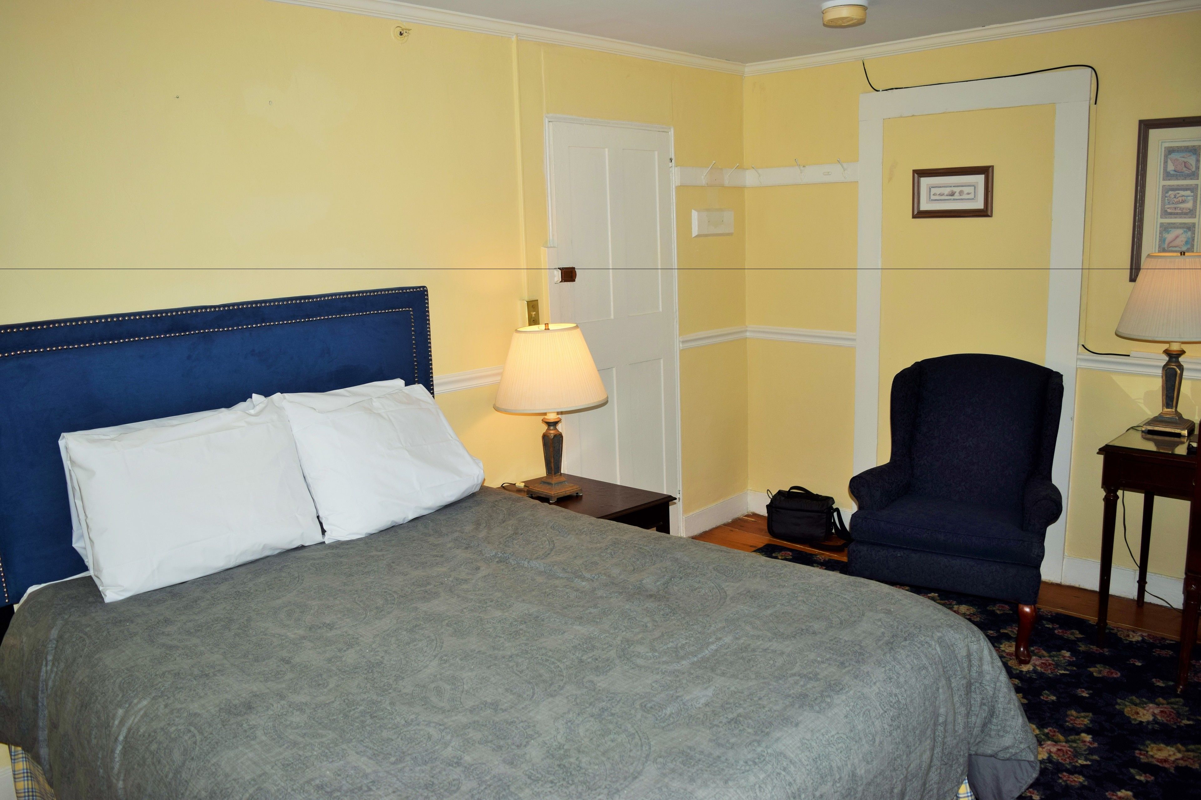 A hotel room with a bed, a chair, a lamp, and a door.