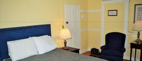 A hotel room with a bed, a chair, a lamp, and a door.