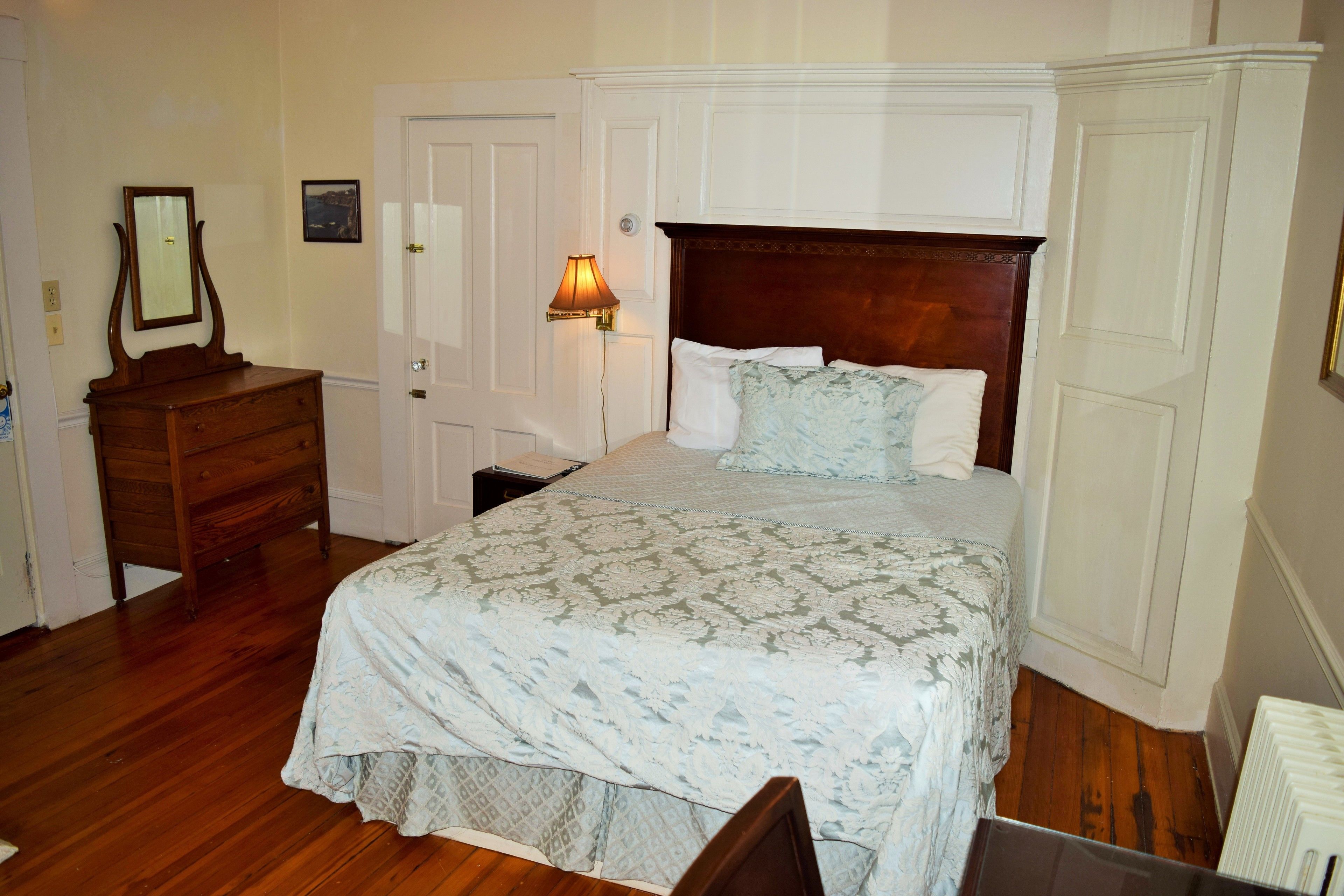 Un dormitorio con una cama de madera, un aparador, una mesita de noche, una lámpara y una puerta.