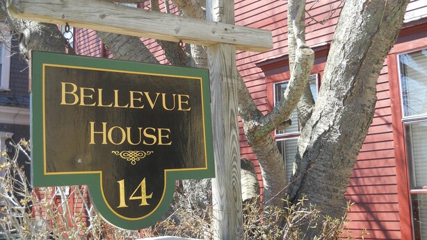 A sign for Bellevue House, number 14, mounted on a wooden post with a red building in the background. - Bellevue House (Newport)