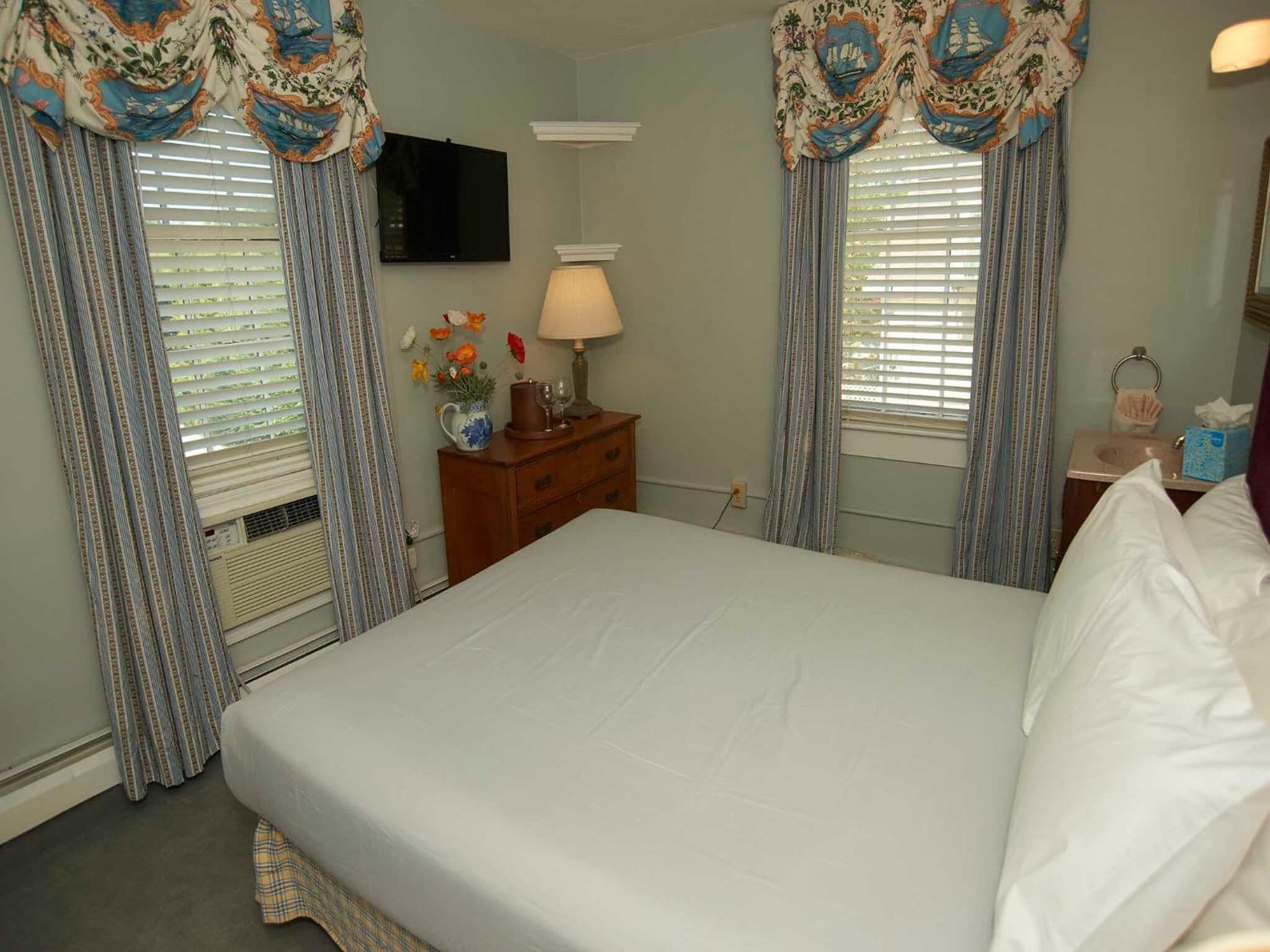 A hotel room with a large bed, a wooden nightstand, a lamp, and a TV on the wall.