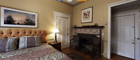 A bedroom with a tufted headboard, a framed painting, a fireplace, and a door.