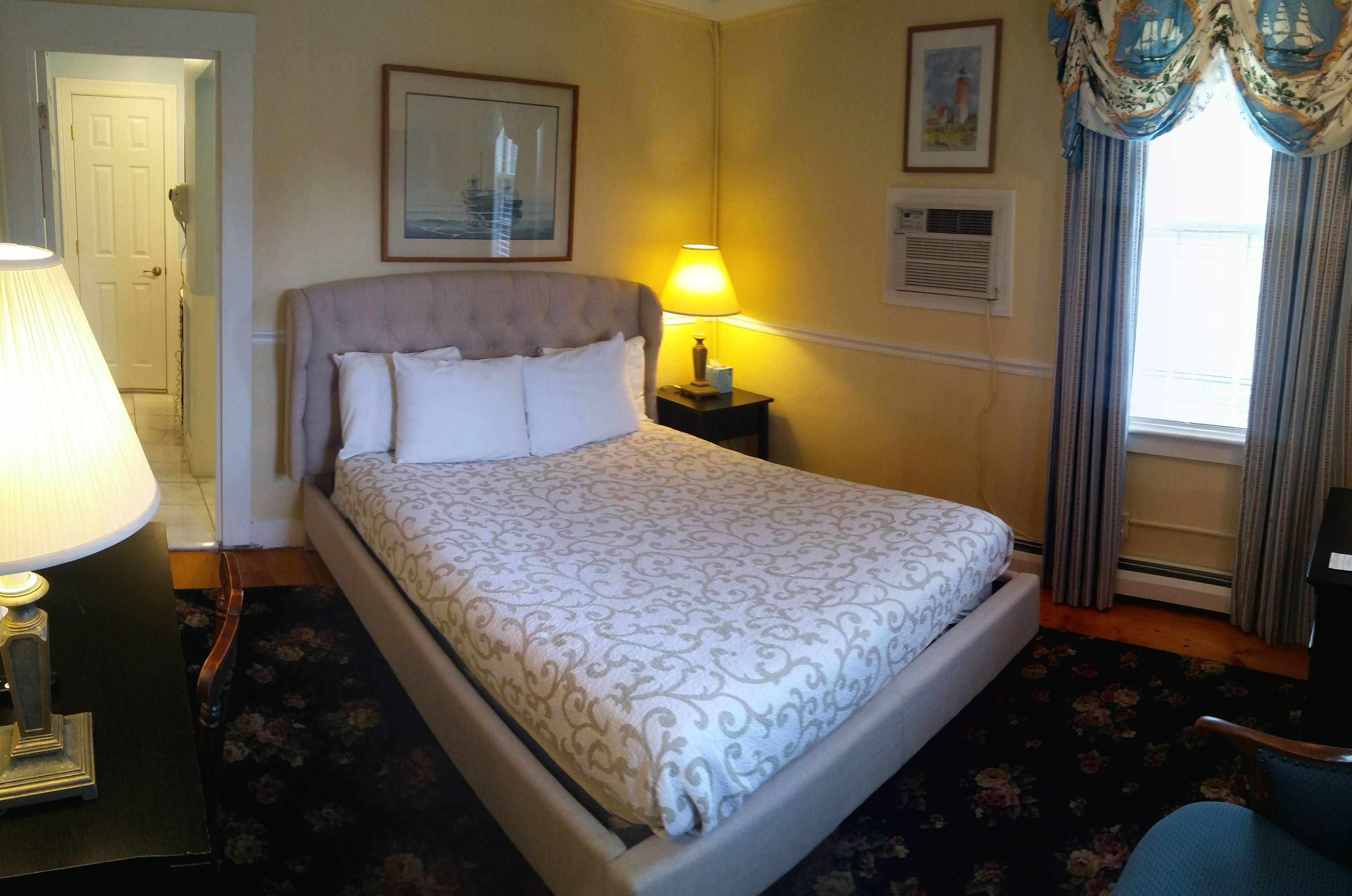 A neatly made bed with a patterned bedspread, a bedside lamp, and a framed picture on the wall.