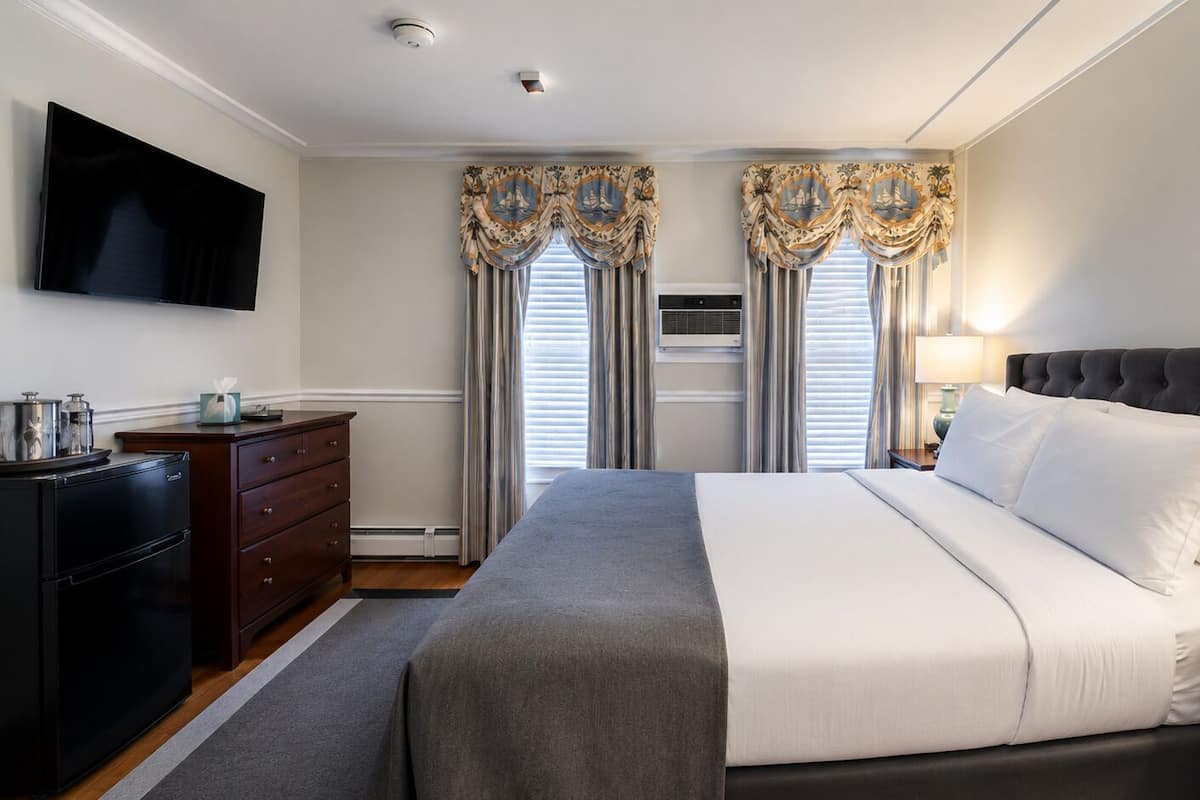 A hotel room with a bed, a TV mounted on the wall, a dresser, and a window with curtains.