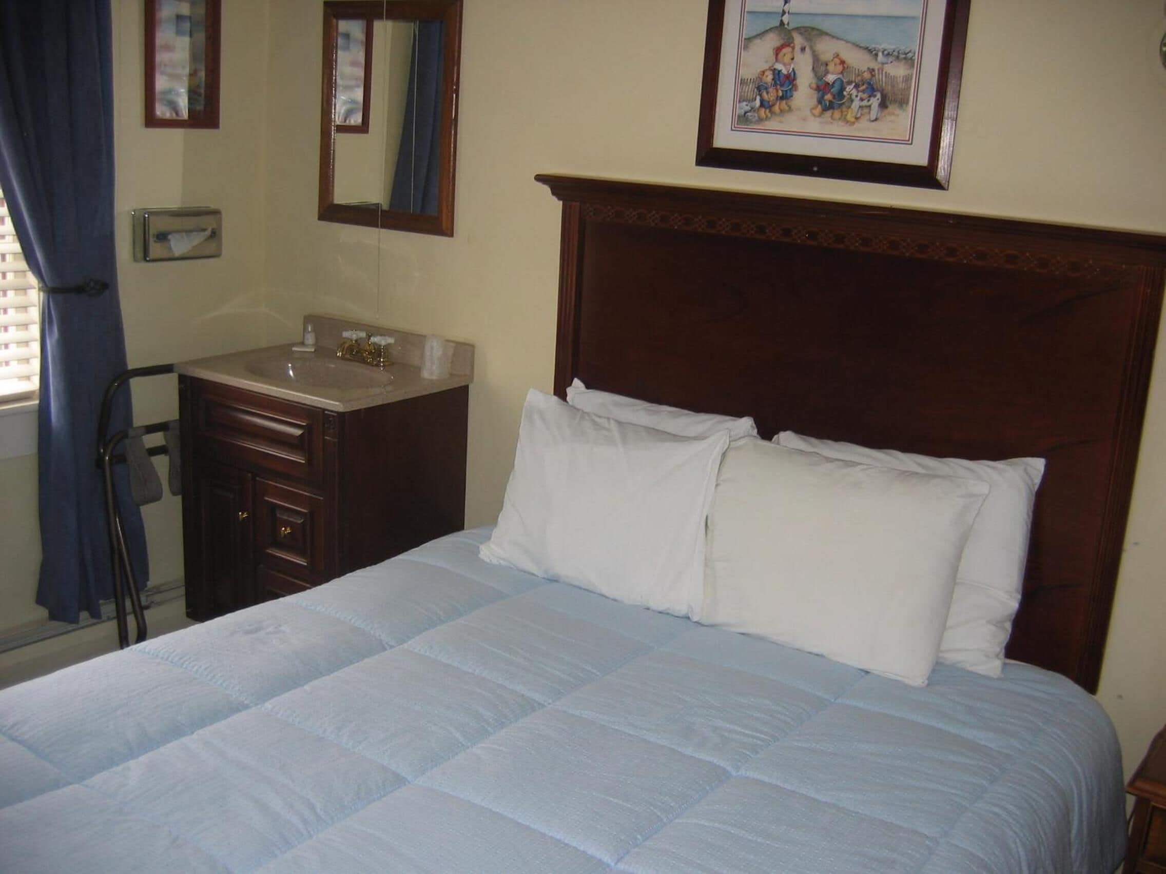 Una cama bien hecha con ropa de cama blanca, un cabecero de madera, una mesita de noche, un espejo y un cuadro en la pared.