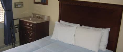 Una cama bien hecha con ropa de cama blanca, un cabecero de madera, una mesita de noche, un espejo y un cuadro en la pared.