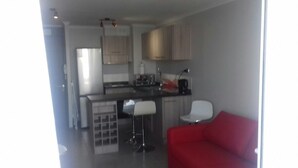 A modern kitchen with white cabinets, a black countertop, and a red couch in the living area. - Depto La Herradura Coquimbo 974 (Coquimbo)