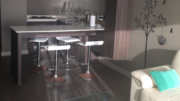 A modern kitchen with a central island, bar stools, and a glass coffee table with decorative items. - Depto Laguna del Mar La Serena 975 (La Serena)