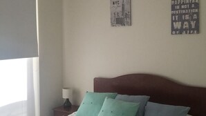 A bedroom with a bed, pillows, a nightstand, a lamp, and two wall decorations. - Depto Laguna del Mar La Serena 975 (La Serena)
