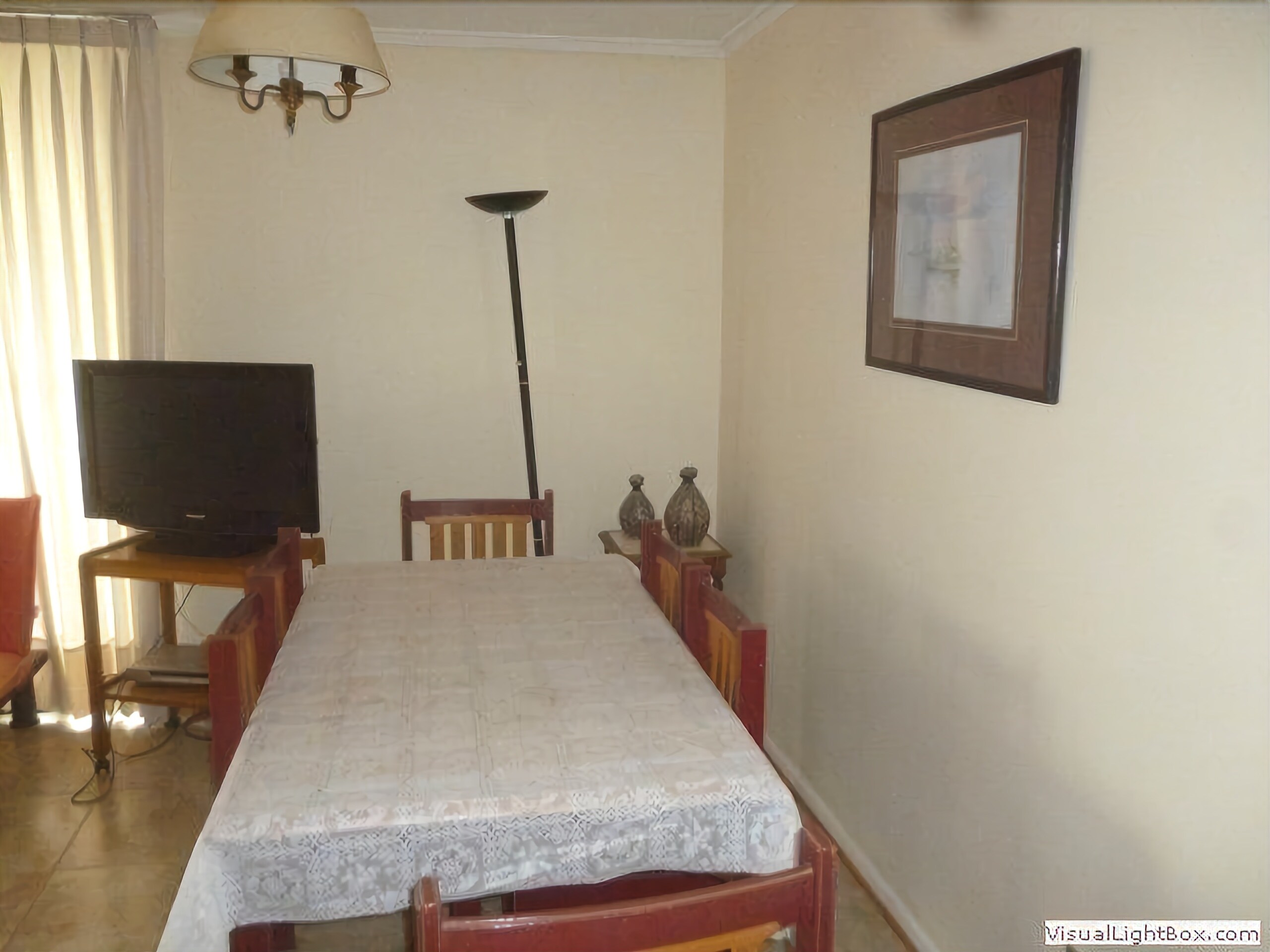 Une pièce avec un téléviseur posé sur un meuble, une table à manger avec des chaises, un lampadaire et un tableau encadré accroché au mur.
