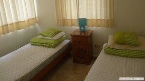 A room with two single beds, each with green-striped pillows, a wooden nightstand with a teal box, and sheer curtains. - Depto Centro Algarrobo 1029 (Algarrobo)