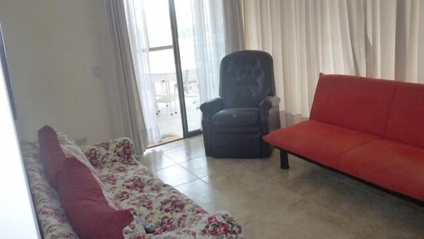 A living room with a red sofa, a floral-patterned couch, a black armchair, and a sliding glass door leading to an outdoor area. - Depto Centro Algarrobo 1029 (Algarrobo)