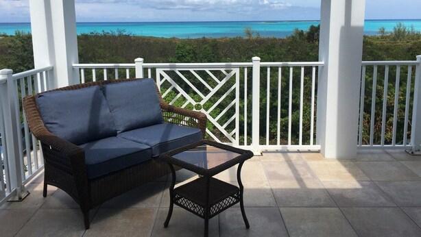 A covered outdoor area with a wicker sofa and a glass table, overlooking a turquoise sea and greenery. - Blue Orchid Villa (Moss Town)