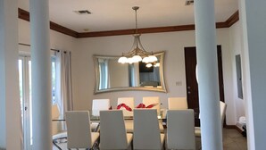 A dining area with a large table, four chairs, a chandelier, and a mirror above the table. - Blue Orchid Villa (Moss Town)