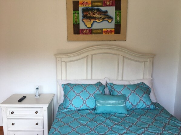 Una cama bien hecha con ropa de cama estampada, una mesita de noche con un teléfono y una obra de arte colgada en la pared.