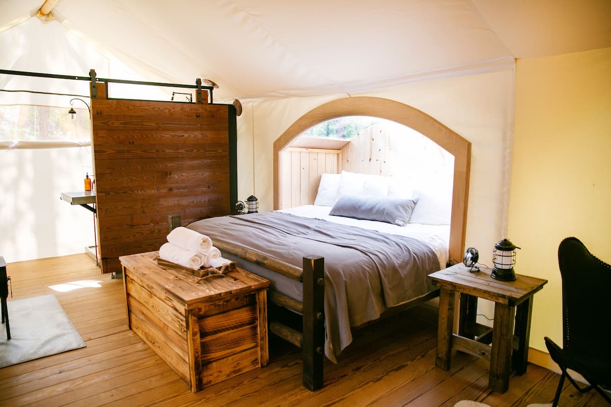 Habitación con tienda de campaña, cama, banco de madera y una pequeña mesa con un farol.