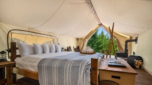 Habitación con tienda de campaña, cama, escritorio de madera y vista a árboles.