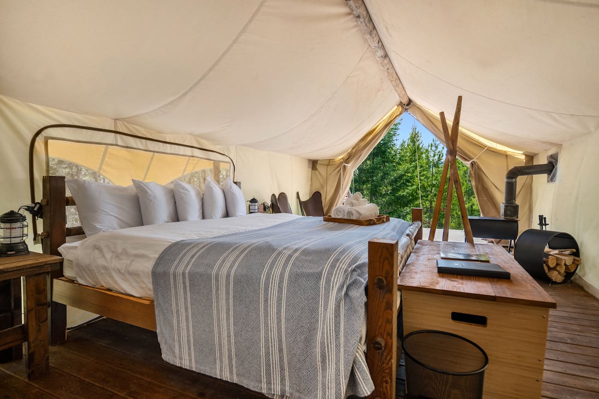 Habitación con tienda de campaña, cama, escritorio de madera y vista a árboles.