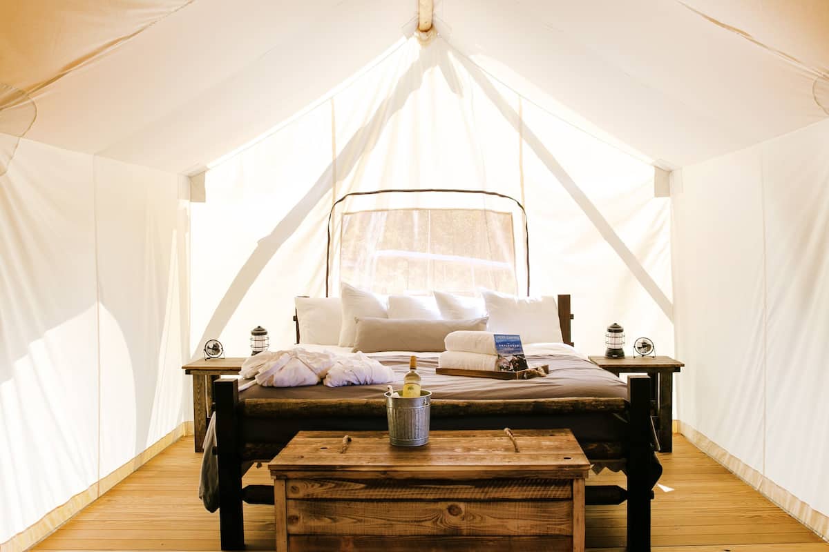 Un alojamiento en carpa con cama, mesitas de noche y un banco de madera.