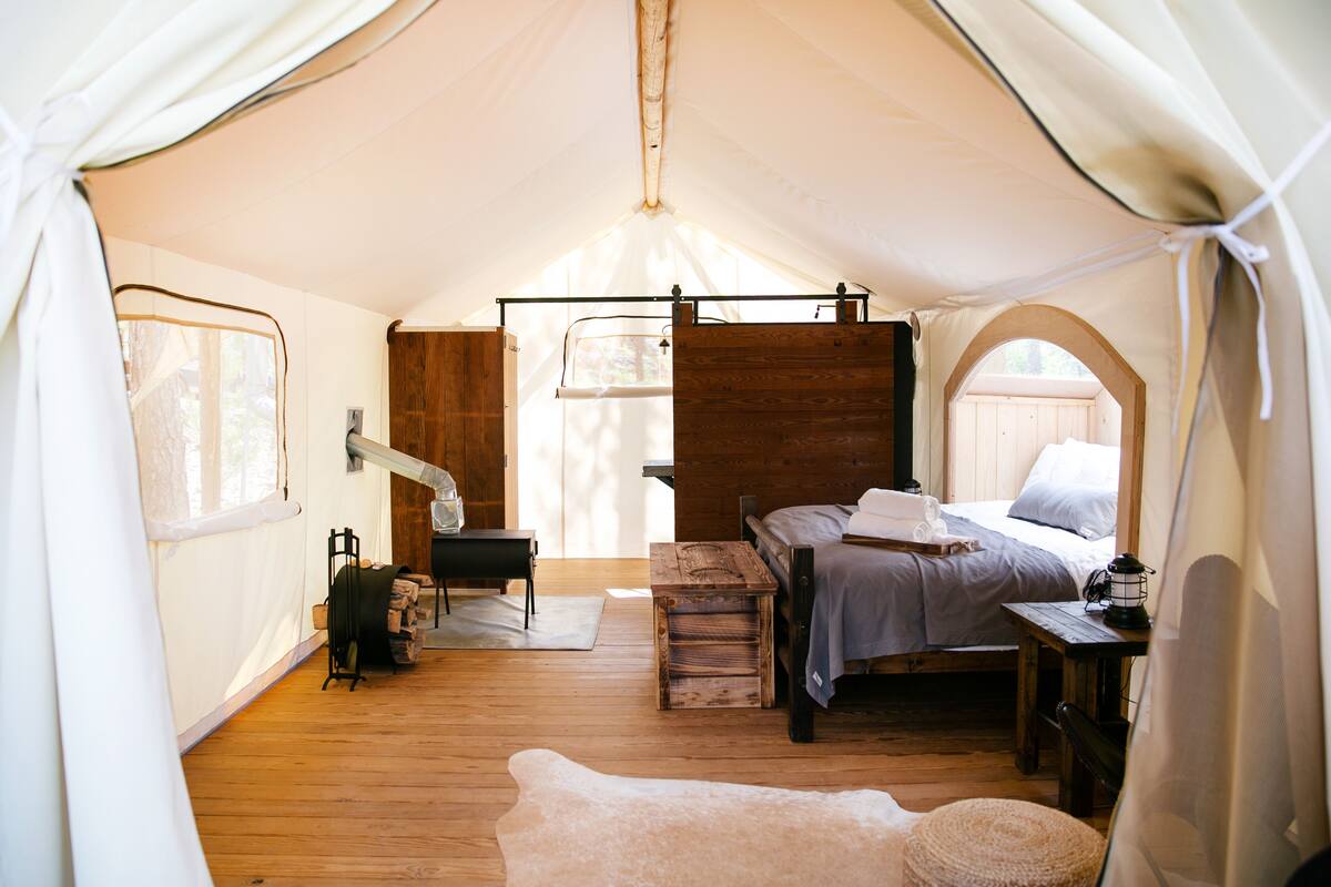 Una habitación con carpa, una cama, un banco de madera, una mesa y una lámpara colgante.