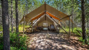 Une grande tente en forme de « A », avec une table et des chaises au centre, entourée d’arbres.