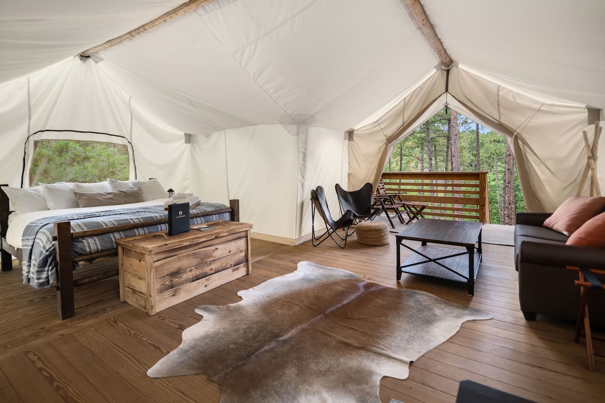 Alojamiento con carpa, una cama, muebles de madera, una alfombra de cuero y vistas a árboles.