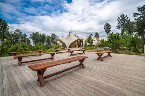 A wooden deck with picnic tables and a unique building with a conical roof. - Under Canvas Mount Rushmore (Keystone)