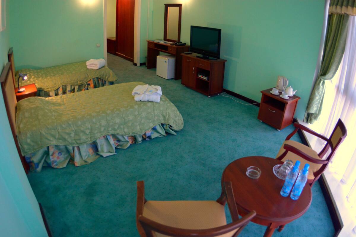 Ein Hotelzimmer mit zwei Einzelbetten, einem Fernseher, einer kleinen Kühlbox, einem Schreibtisch und einem Stuhl.