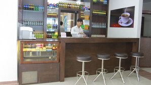 Un espace bar avec des étagères remplies de boissons, un réfrigérateur-vitrine et trois tabourets.